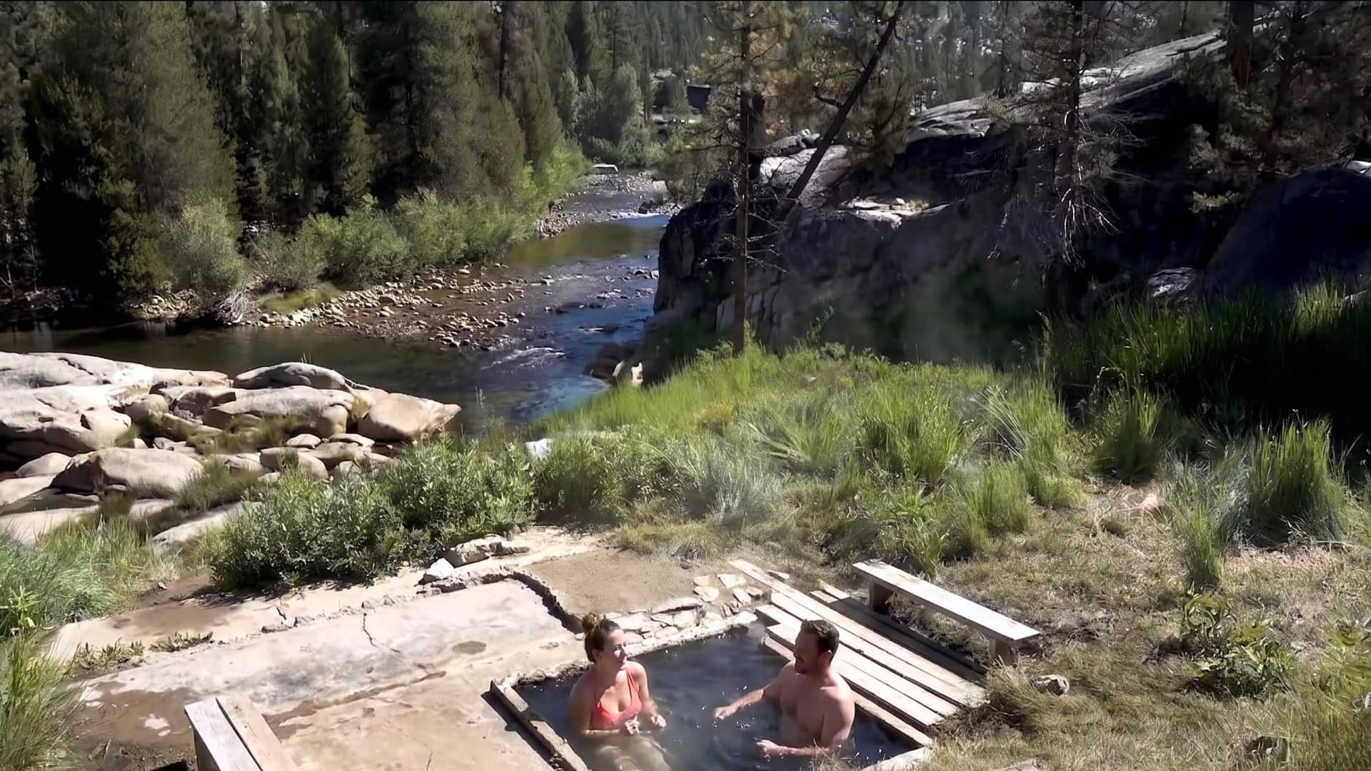 Couple relaxing together in a natural mineral hot spring pool surrounded by granite rocks and pine forest at Mono Hot Springs