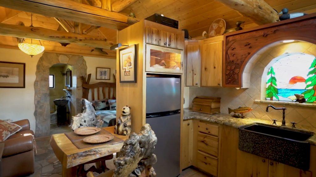 Interior of the Mono Hot Springs Honeymoon Cabin showing the open kitchen, stained-glass window, log beams, and cozy living area