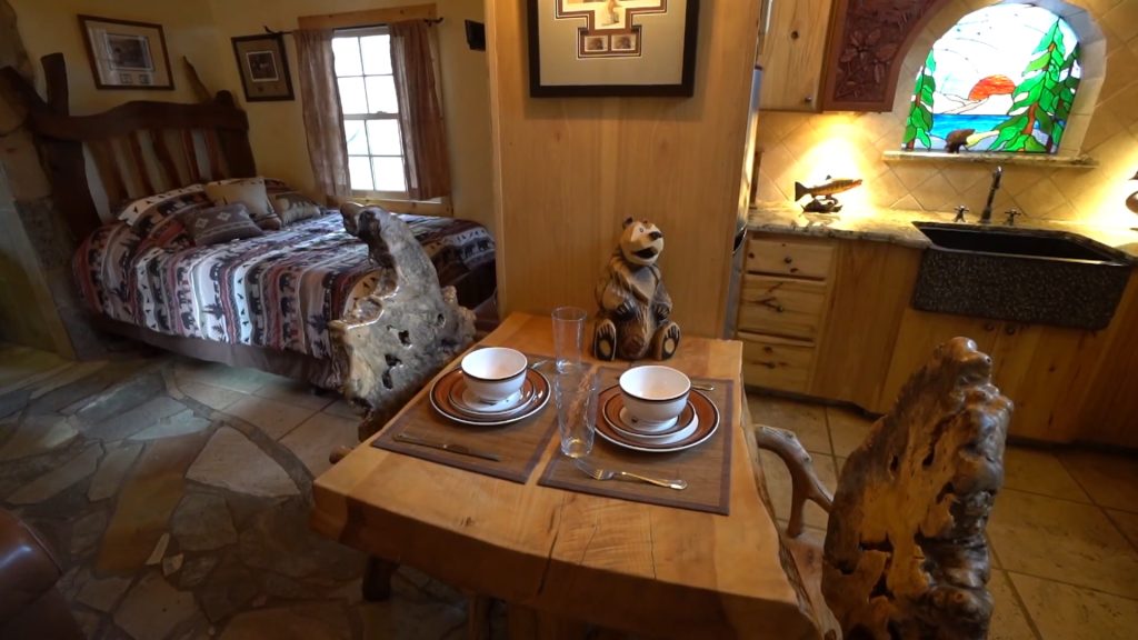 Honeymoon Cabin bedroom with a rustic log bed, set dining table, and stained-glass kitchen window at Mono Hot Springs Resort