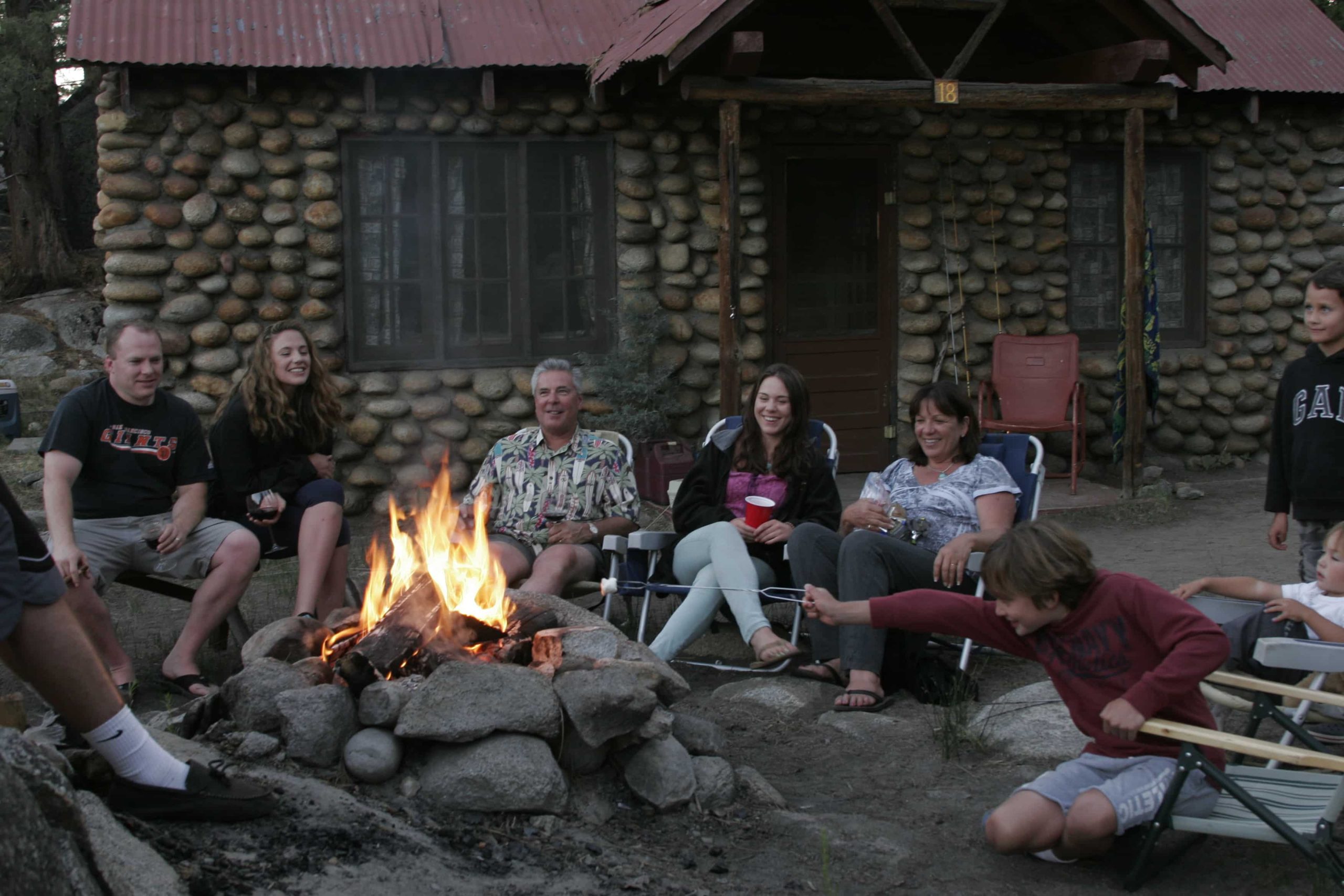 Family roasting marshmallows around a campfire in front of a historic stone housekeeping cabin at Mono Hot Springs Resort